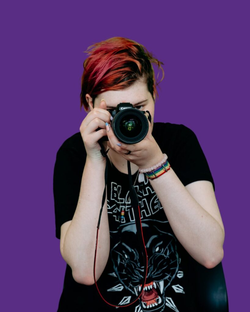 Participant holding a camera. Dressed in black clothing. We belong program