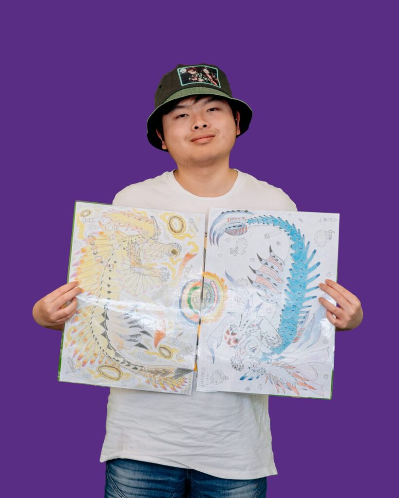 Participant holding artwork. White shirt, bucket hat. We belong program