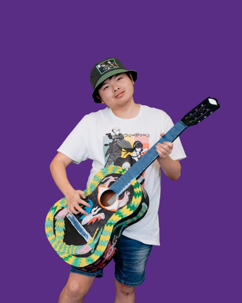 Participant playing guitar. White shirt. Bucket hat. We Belong Program.