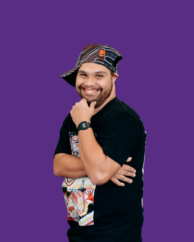 Tel is posing to the side. Side cap. Black shirt, blue pants. We belong program